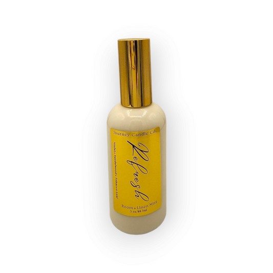 Refresh room and linen spray in a white jar with a sleek gold lid, featuring bright lemon, crisp cotton, and green leaves – a fresh, uplifting home fragrance mist